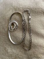 Photo showing two silver bracelets: one flat snake chain and one figaro link chain, alongside a pair of rounded hoop earrings.