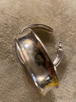 Pair of large silver hoop earrings laid on a soft fabric surface, showing thickness and curvature.