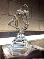 Side angled view of the glass figurine showing the woman's posed figure and layered pedestal base.