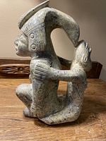 Angled profile view of stone sculpture showing human figure with headdress and arching form