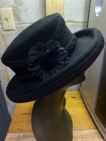 Black ladies designer hat shown from side angle focusing on flower decoration and braided trim.