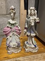 Male and female porcelain figurines in Rococo style placed side by side on a wooden surface showing full figure and bases.