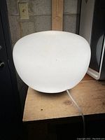 White globe lamp on wooden surface, front angled view showing smooth round shape and power cord.