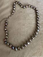 Full view of pearl necklace arranged in a heart shape showing the irregularly shaped grey and silver pearls and silver clasp.