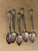 Top view showing the intricate decorative scroll and floral handle designs of all five teaspoons.
