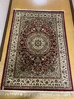 Full view of the Turkish rug showing the central floral medallion in red, cream, and green colors with a floral border and fringed edges.