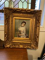 Front view of Victorian oil painting in ornate antique gold frame showing woman holding flowers