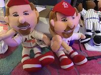 Two plush dolls of Mark McGwire in St. Louis Cardinals uniform with #25 sitting side by side on a surface. Both dolls have original tags attached and have an embroidered facial design.