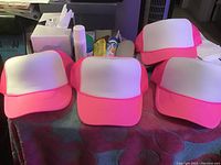 4 pink and white mesh caps with pink bills and mesh backs, white front panel, displayed on table