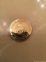 Photo of the gold tone commemorative coin showing the front side with 50th Anniversary, Service Excellence, and Established 1939 embossed.