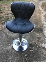 Bar stool photo showing black padded seat and backrest with triangular pattern, chrome pedestal base with footrest.