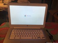 Photo of white HP Chromebook laptop powered on showing Chrome OS loading screen.