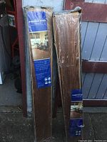Two sealed packages of American Spirit glueless laminate flooring planks standing upright against a wall and gate.