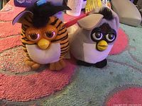 Two Furby toys side by side on a colorful towel background.