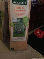 Photo of Gardenline Walk-In Greenhouse in box, showing product image and specifications on packaging.