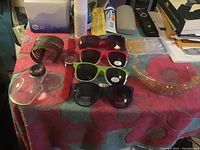 Four pairs of sunglasses, one large cuff bracelet, red watch, gold tiara, and assorted charms displayed on a red patterned cloth.