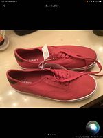 Top view of red canvas men's sneakers with laces, showing size 10 and tags attached, on glossy surface.