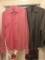 Two men's dress shirts hanging: a pink and white gingham check shirt and a solid dark gray shirt.