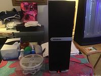 Polaroid Bluetooth speaker standing upright next to LED strip reel and various small items on table.