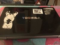 Top view of the Toshiba laptop lid showing sticker decals and some wear.