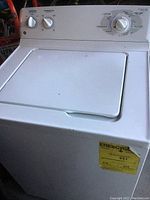 Photo of a white top-loading washing machine with a missing control knob and energy guide label on front.
