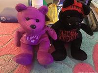 Two plush bears: one purple with 'Luvvy' embroidery and one black with red WCW hat and shirt sitting on a carpet