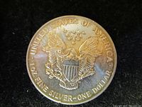 Photo of reverse of the 1991 US Silver Eagle coin showing heraldic eagle with shield, surrounded by inscriptions and stars.