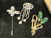 Three costume jewelry pieces on black velvet: butterfly stick pin, clear rhinestone dangling brooch, green rhinestone Coro brooch