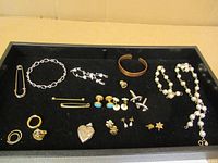 Full tray view showing jewelry items including earrings, bracelets, cufflinks, a necklace, and a heart locket pendant on black background