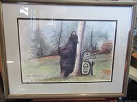 Framed limited edition print showing a black bear climbing a tree with indigenous art symbol, signed by Sue Coleman.