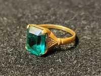 Front angle close-up of gold ring with green faceted rectangular stone on black background.