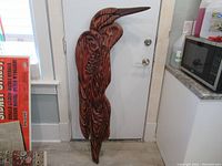 Full front view of carved wooden heron leaning against a door, shows overall shape and size