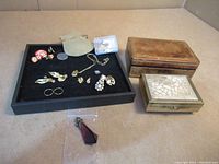 Full lot layout showing assorted earrings, rings, pendants on a black tray next to two vintage jewelry boxes