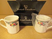 Pair of Royal Doulton Autumn's Glory coffee cups with original box in the background, one cup wrapped in protective plastic.