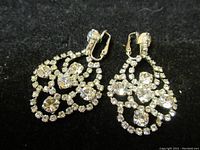 Pair of vintage Sherman rhinestone earrings on black background displaying design and rhinestones.