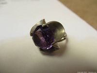 Close-up of silver ring showing purple faceted stone and decorative setting.