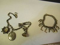 View of both bracelets laid flat on a white background. Shows the charm bracelet with three charms and the costume bracelet with metal letters.