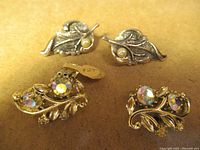 Top view of two pairs of vintage MCM-style costume jewelry earrings on a tan background, one with pearl accents, the other with aurora borealis rhinestones.