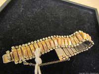 Full view of vintage 1960s Kramer bracelet showing rectangular marbled orange stones set in silver-tone metal linked base with clear rhinestones on edges, laid on black velvet box.