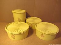 Four vintage yellow Tupperware containers with lids arranged on brown background showing overall lot presentation.