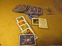 Overall view of two sets of playing cards, one with blue backs laid out on the table, showing multiple cards, and one deck with a more traditional back design in the corner.