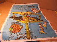 Full view of the blue linen tea towel showing colorful birds on bird table and feeder with tree branch backgrounds.