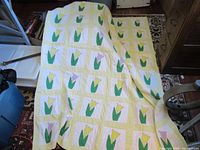 Quilt fully visible displayed on a stand, showing the repeating floral pattern with yellow and purple tulips on white and yellow backgrounds.