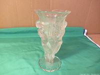 Full view of the Lalique frosted glass vase with three nude female figures around the body and faceted base sitting on a green cloth background.