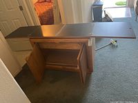 Rustic wooden buffet cabinet with two doors open and fold-out top extended, showing interior storage space