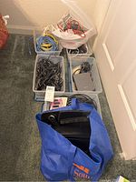 Overview photo showing multiple bins and bags filled with various electronic cables and adapters arranged on carpeted floor.