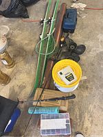 Full view of fishing and outdoor items including skis, rods, nets, tackle boxes, bucket with fishing line, and propeller parts.