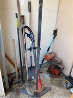 Overview of garden tools including shovels, weed eater, and other equipment in a garage corner.