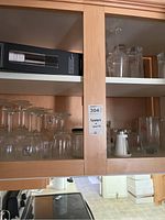 Upper cabinet with glassware items including wine glasses and cubes, electric wine opener in box, and various cups and mugs.