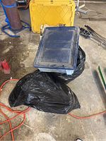 Two black plastic bags and a yellow plastic storage bin visible in garage setting; hats not visible in this photo